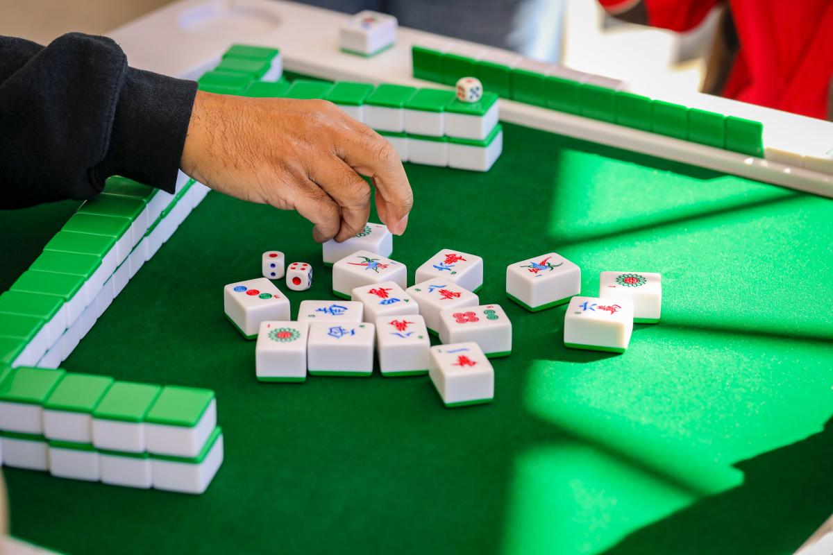Image of person's hand reaching out towards mahjong tiles on a green table