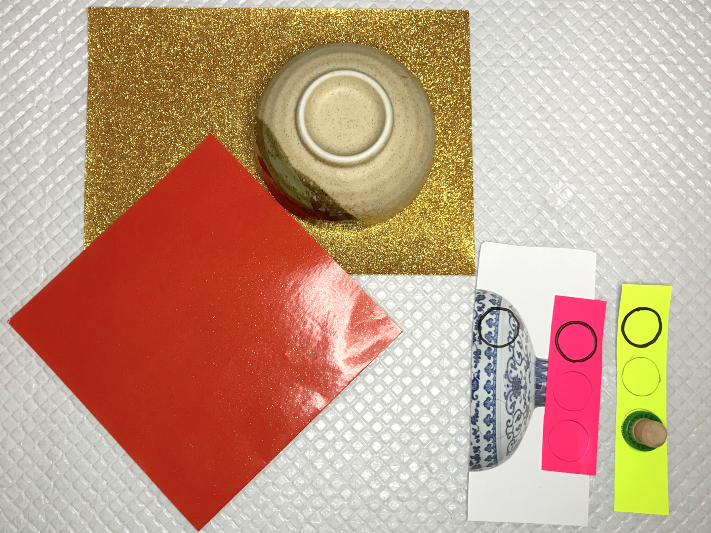 A square piece of red paper. A bowl on top of gold paper to be drawn around. Small pieces of paper with small circles drawn on.