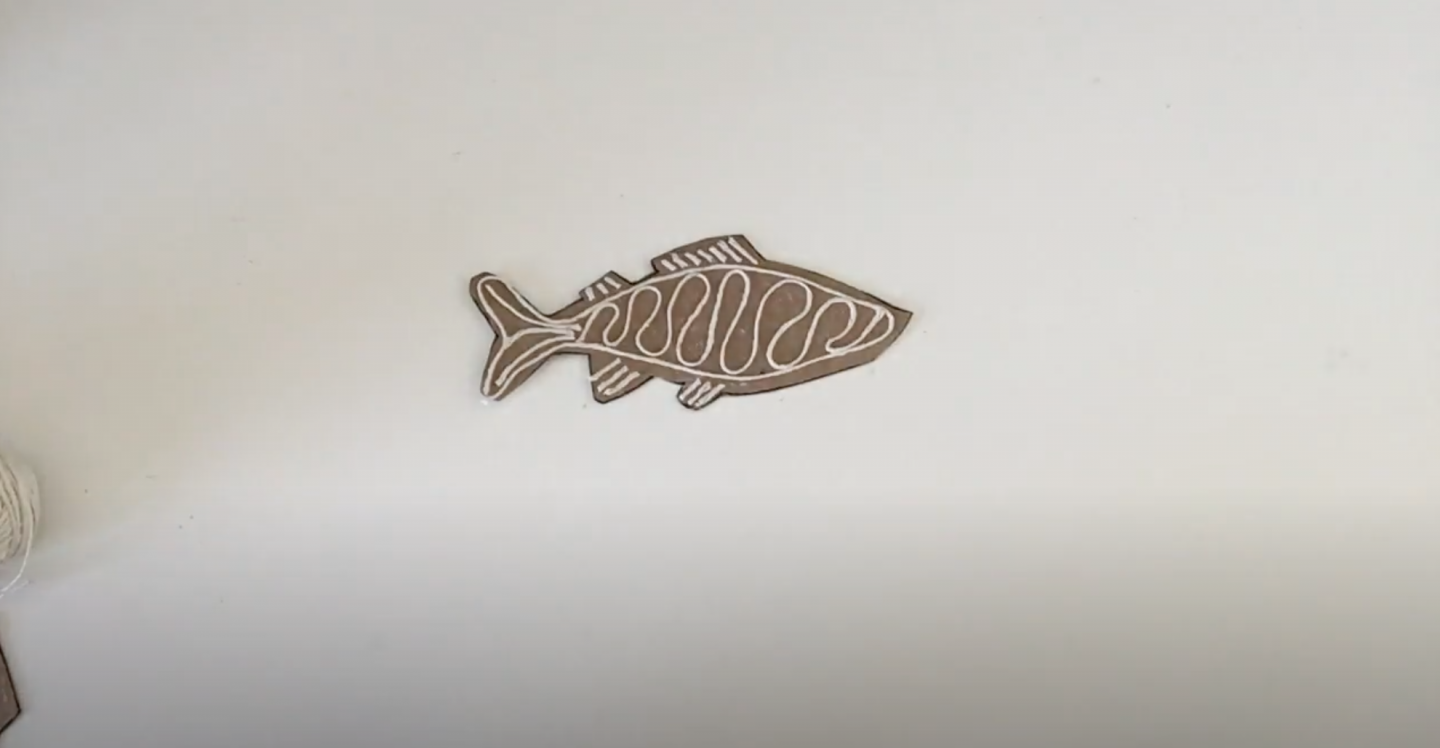 cut out cardboard fish with string stuck to surface