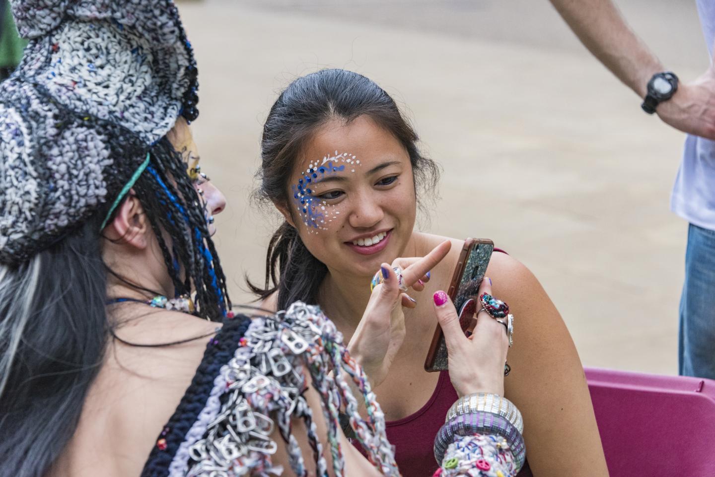 A young person with their face painted looks at an image of their face