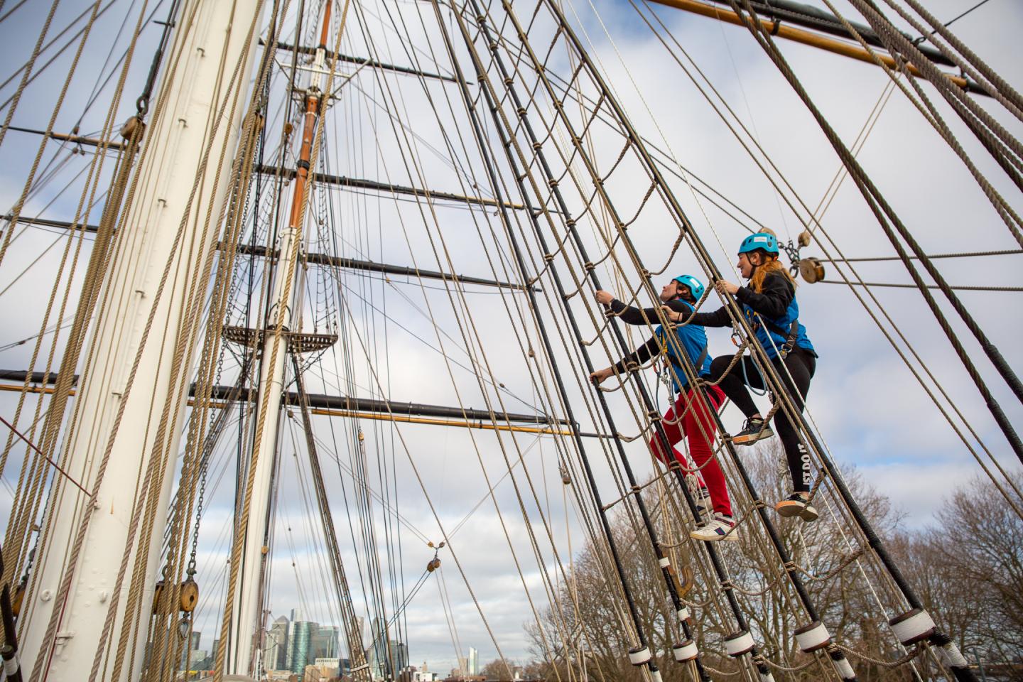 The image shows two people ascending the rigging of the Cutty Sark.