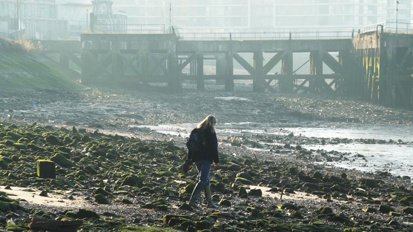 Image of woman walking on Thames foreshore with Enderby Pier in background