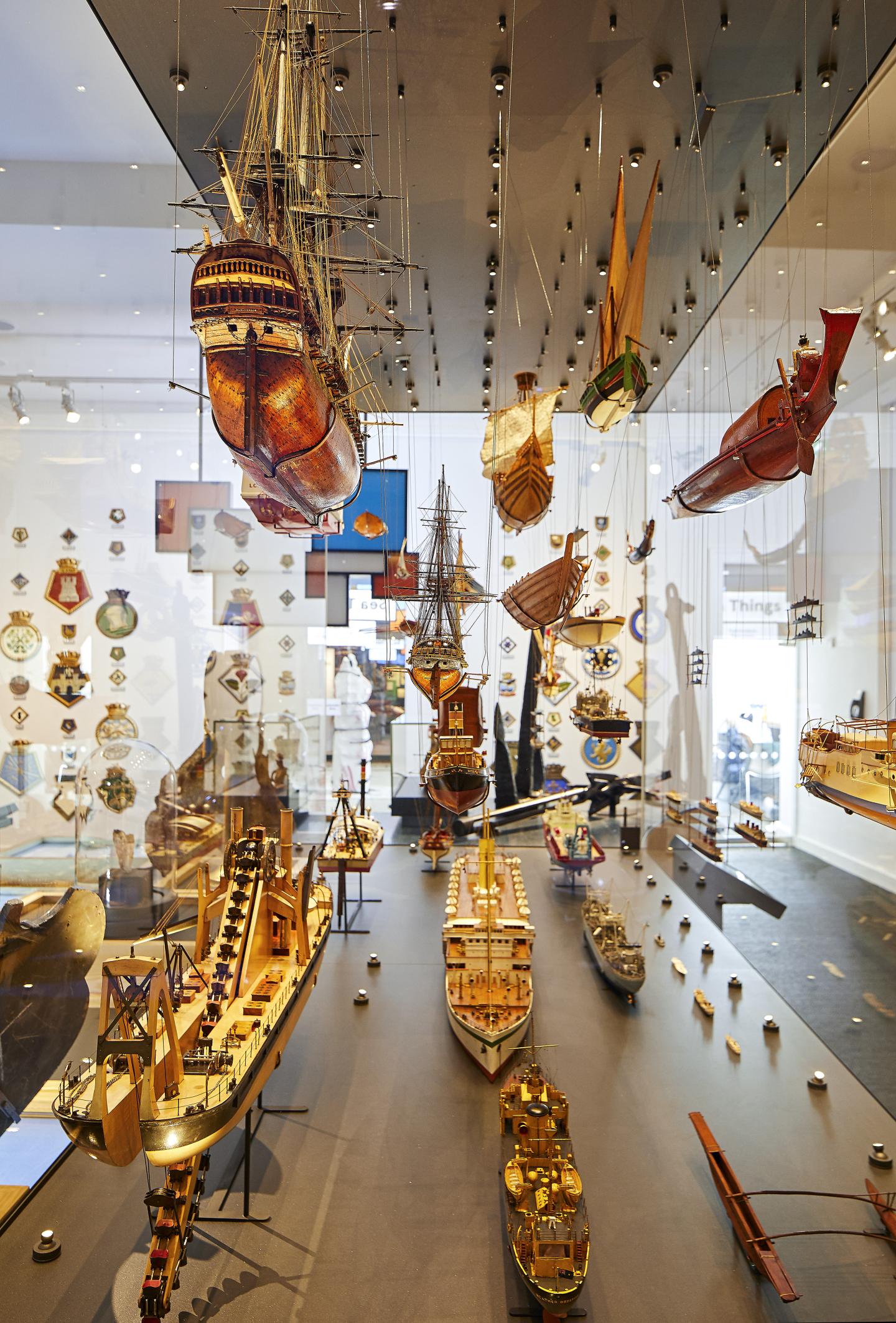 An image showing multiple wooden ship models depicting a range of different types of boats and vessels hanging or on the display bottom which is surrounded by glass