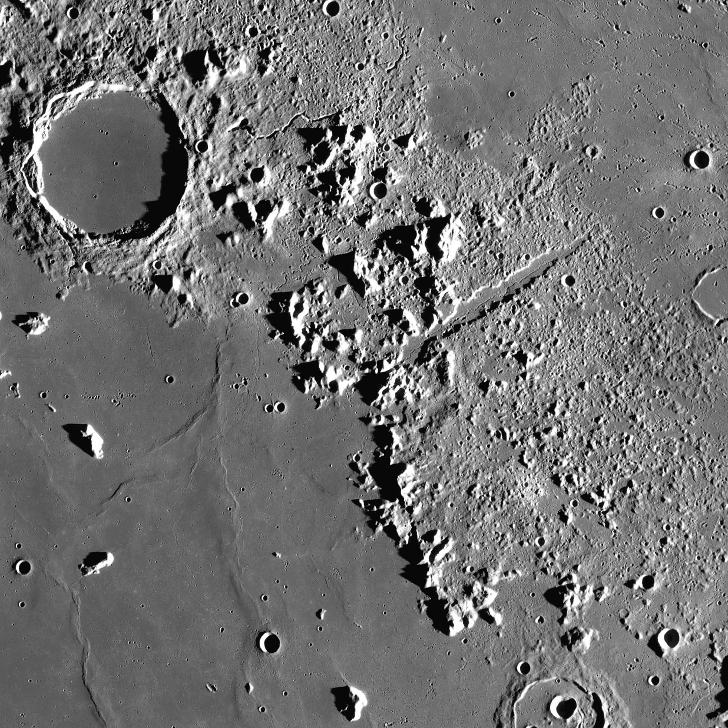 Photo of the lunar surface showing a circular crater and a mountain range
