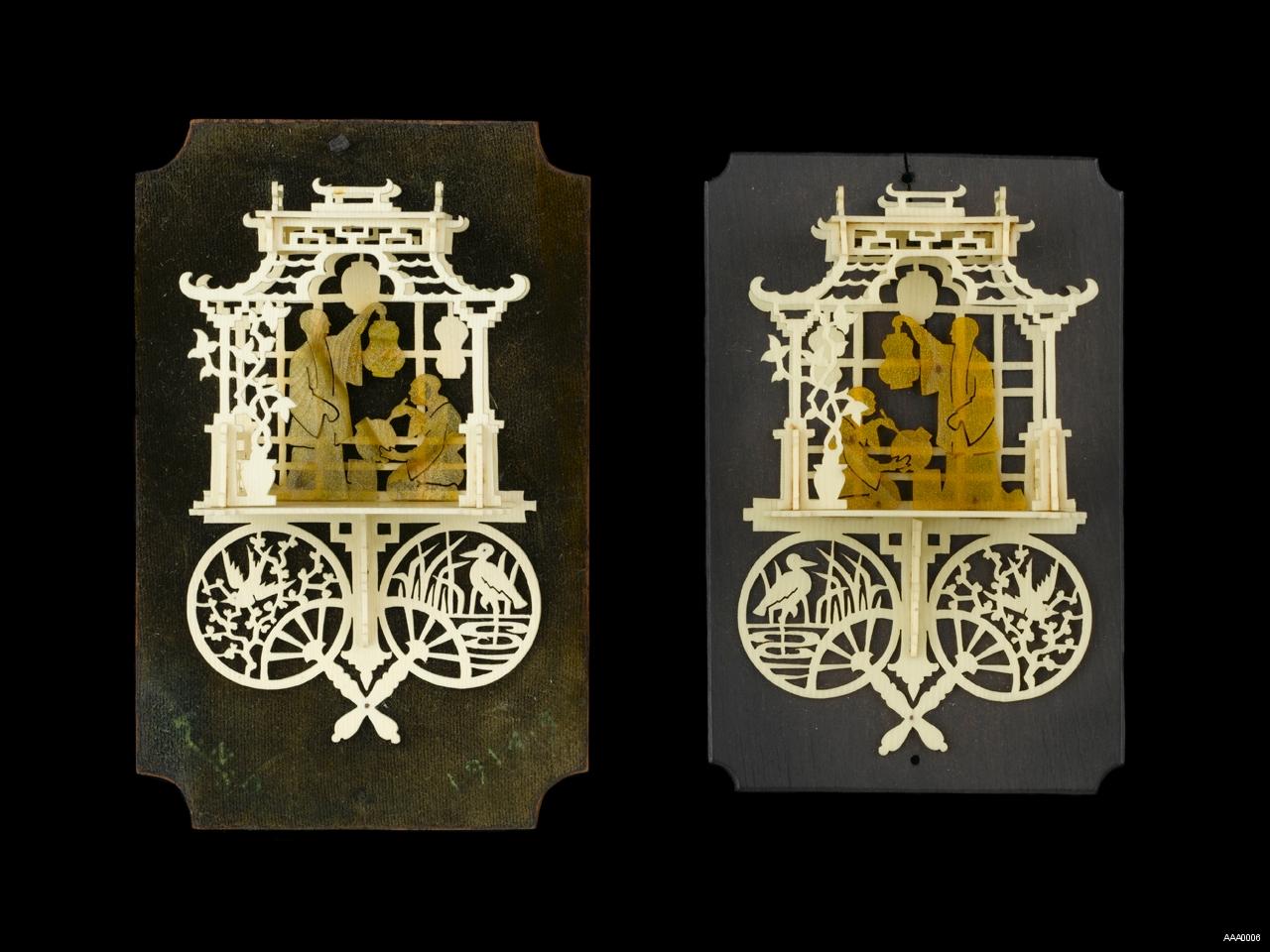 A pair of bonework plaques depicting fretwork Chinese pavilions. Two figures are hanging up lanterns inside each pavilion and beneath are two crossed fans depicting a heron and a bluebird.