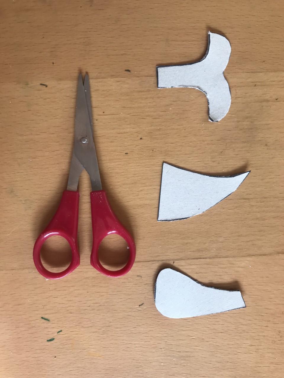 Cut out your tail and fins Three shapes cut from cardboard lie next to a pair of red scissors. They are shaped like a whale tail and two fins.
