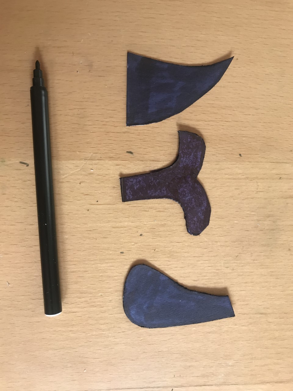 Colour them in Three cut outs, 1 in the shape of a whale tail and 2 in the shape of fins, are coloured black. The pen lies nearby.