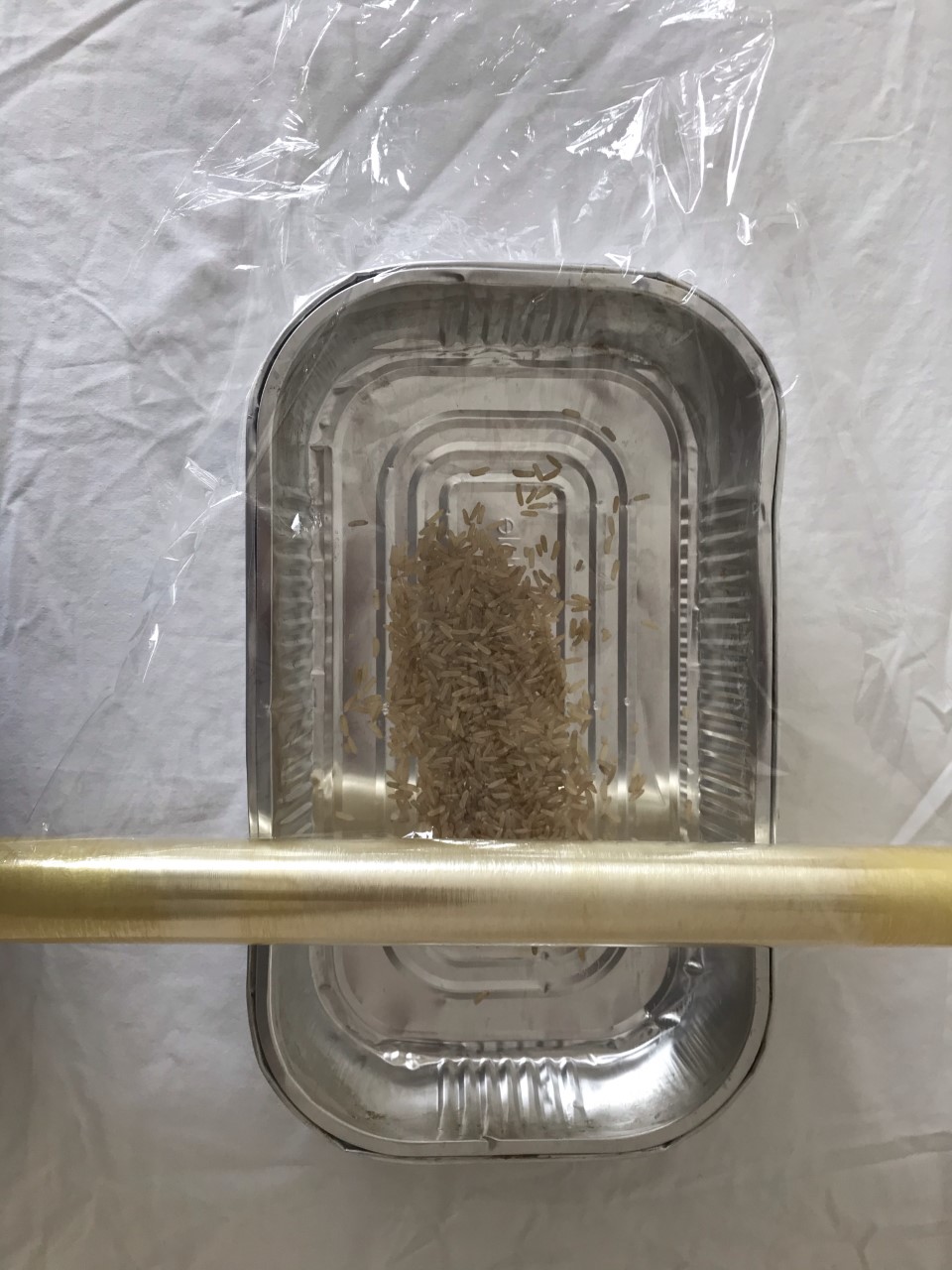 Measure your cellophane A metal tray with rice inside. Cellophane is being measured out to cover the top of the tray.