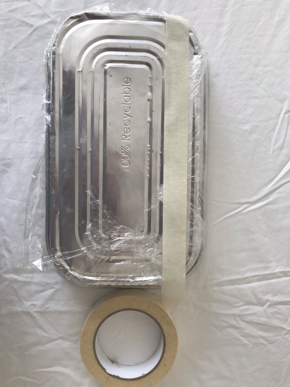 Stick the clingfilm down. Clingfilm is being stuck to the bottom of a metal tray using tape.