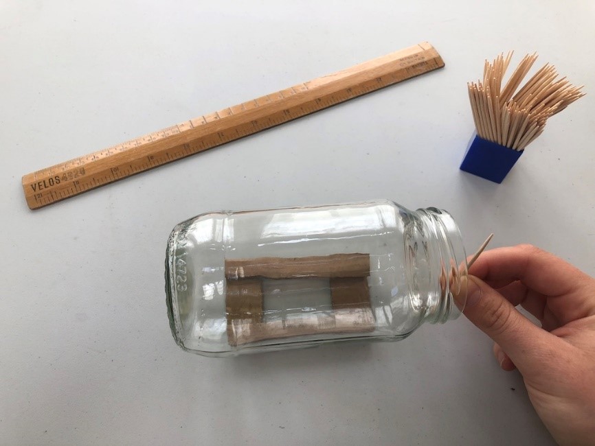 Make your masts An empty jar lies on it's side on top of a stand made of cardboard. Someone hold a toothpick beside the jar to measure it's height.