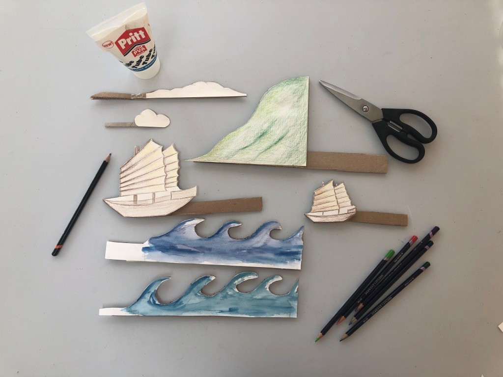Create your props Drawings of two Junk ships, a wave, clouds and a cliff with cardboard handles are on a surface. Pencils, scissors and glue are nearby.