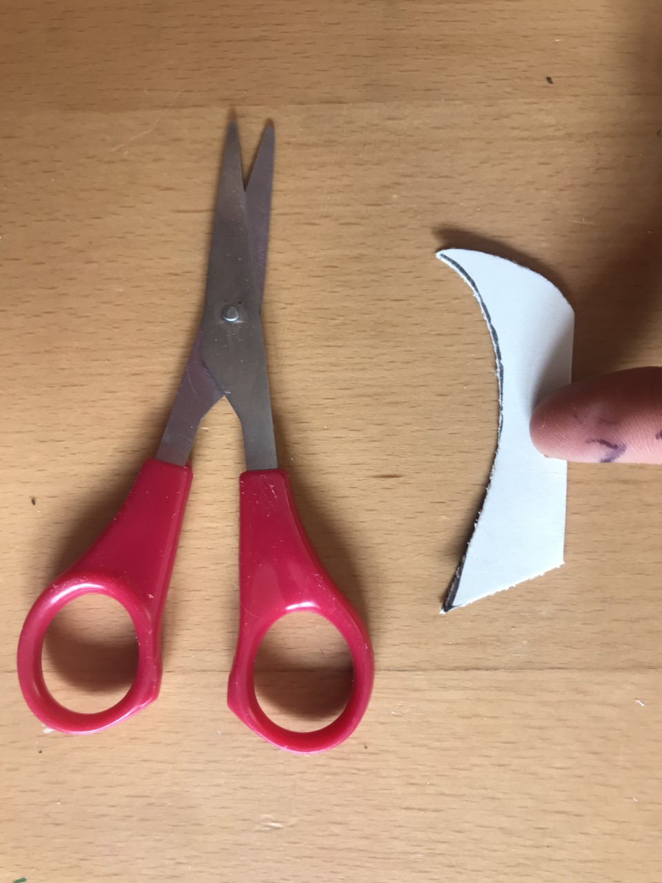 Glue the curved end A pair of red scissors are next to a piece of cut out folded card.