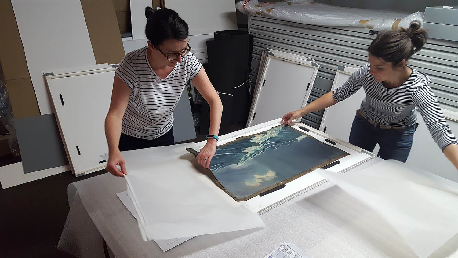Image of Collections Storage Manager and Collections Retrieval Manager rehousing un-stretched oil paintings in custom-made trays Image of Collections Storage Manager and Collections Retrieval Manager rehousing un-stretched oil paintings in custom-made trays