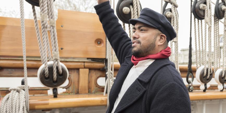 James Robson the cook, one of the characters you can meet on board Cutty Sark. He wears a flat cap and red scarf, and is pointing at the ship's rigging