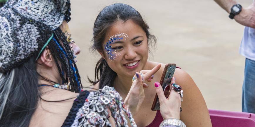 A young person with their face painted looks at an image of their face
