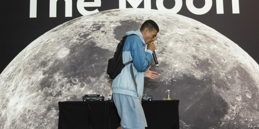 A performer singing into mic in front of image of moon