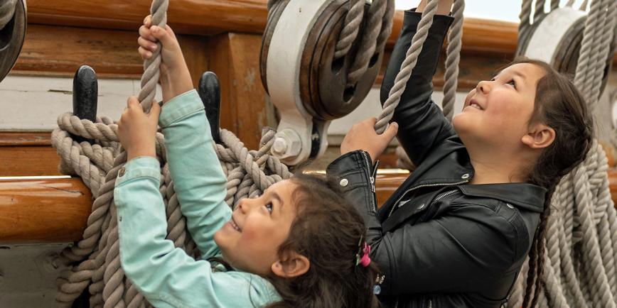 Two young children pull on ropes that act as part of the rigging for historic ship Cutty Sark