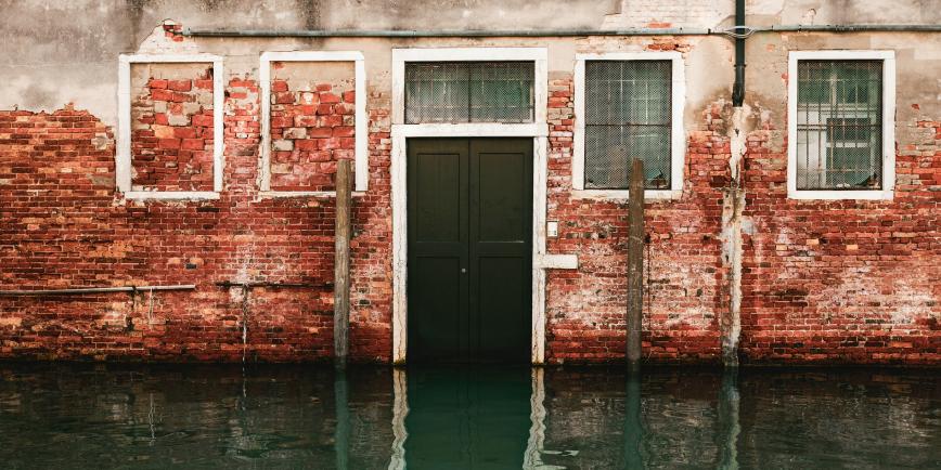 A wall in Venice partially submerged in water. The red bricks are looking damaged