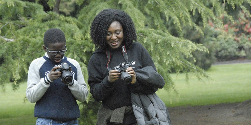 Two people look at their cameras in a park.