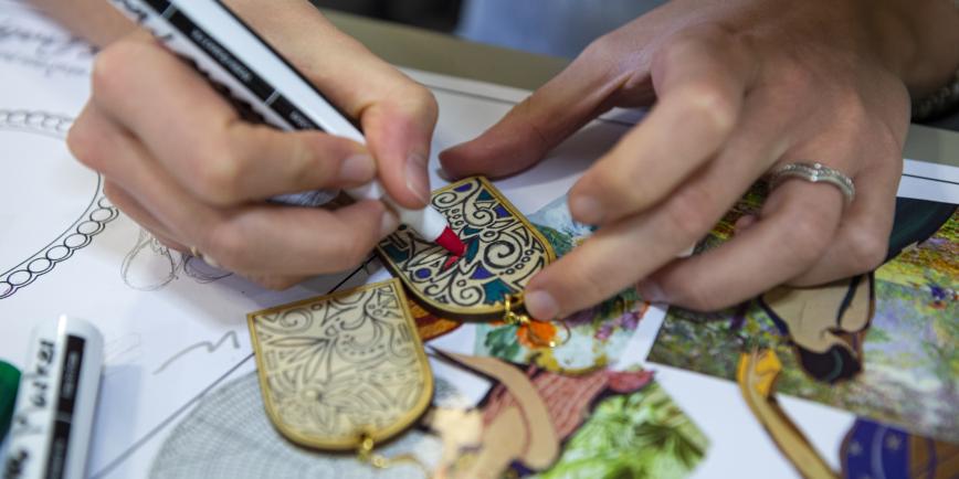 Close-up shot of a person's hands as they use a felt-tip pen to draw an intricate pattern on a small piece of wood