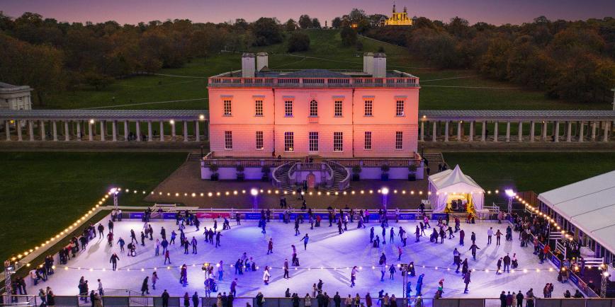 Image of the Queen's House in Greenwich lit in pink lights at dusk, with ice rink in front with lots of people on it, lit up in blue