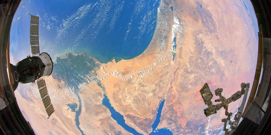 A fish-eye view of Earth taken from a satellite. Yellow and orange desert is visible along with deep blue ocean and wispy clouds