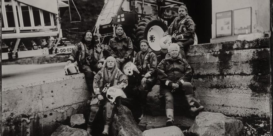 Black and white photograph of a group of lifeboat volunteers sitting on a slipway in front of a tractor