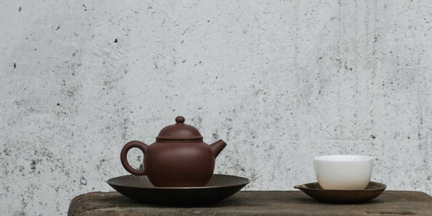 A red clay teapot and white cup on a black saucer, both placed on a table