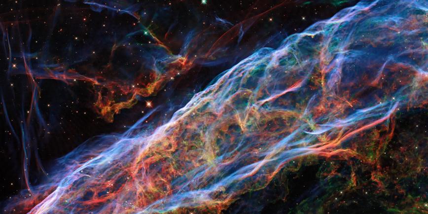 The Veil Nebula as seen by the Hubble Space Telescope. Filaments of blue, green, and red light cover the image, tracing different gases inside the curtain-like cloud.