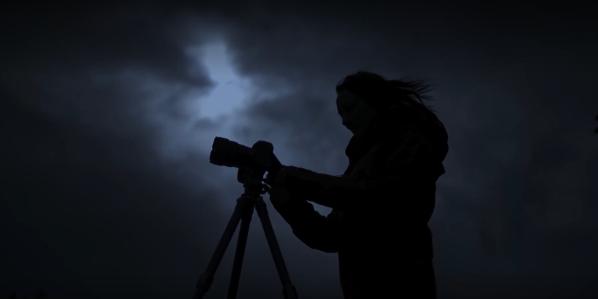 Silhouetted image of woman with camera against a dark sky