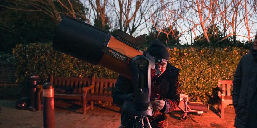 A man leans in to a telescope eyepiece during an evening astronomy event
