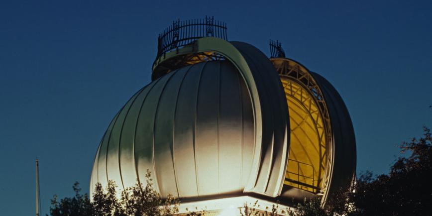 The Great Equatorial Telescope dome of the Royal Observatory Greenwich, lit up at night with a full moon in the sky above