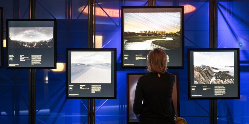 A woman, with her back to the camera, looks at a number of astronomy photographs lit up on large illuminated display screen