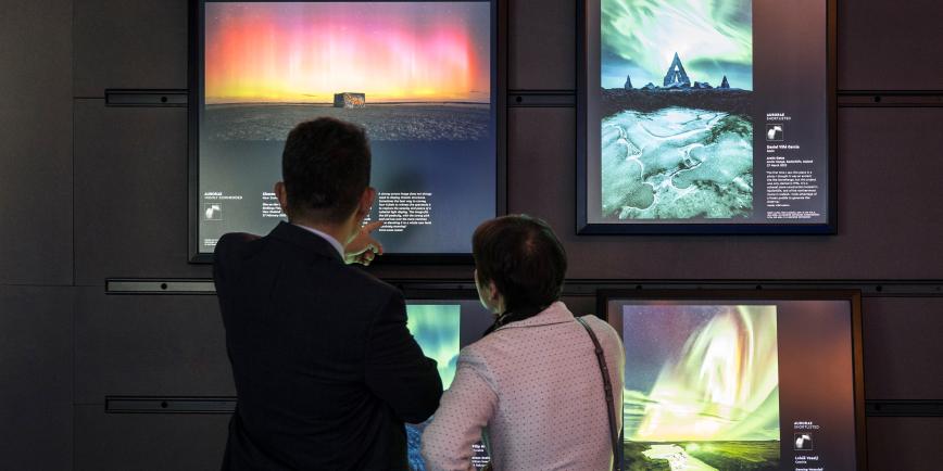 A man and a women, with their back to the camera, look at a series of astronomy photographs on large illuminated display screens
