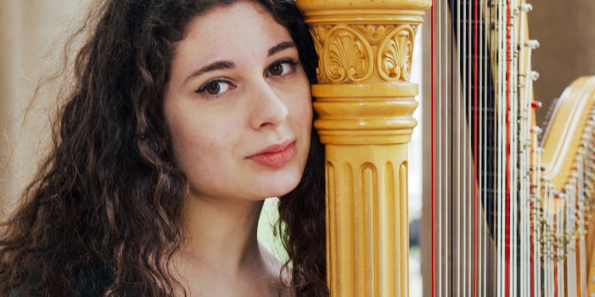 Profile photograph of harpist Lucia Foti. She has dark curly hair and her head is leaning against a large golden harp