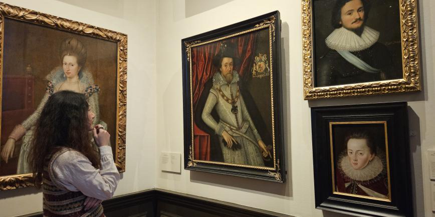 A woman gazes at portraits of historic figures. Three paintings are displayed in a gallery in front of her
