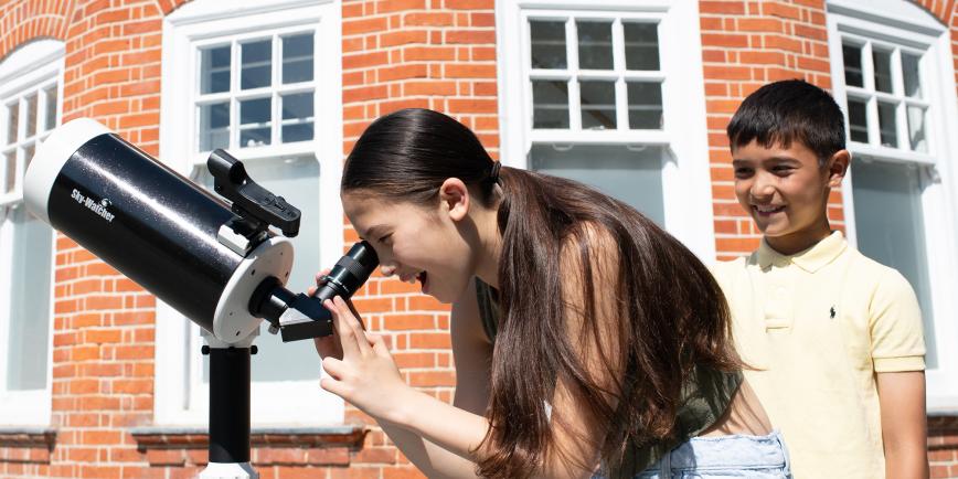 A girl looks through a telescope at the Royal Observatory, as her brother looks on