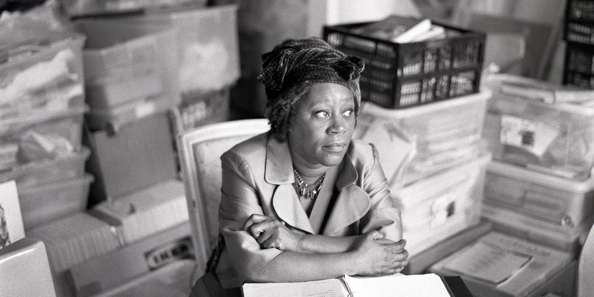 Black and white photograph of artist Sonia Boyce sitting at a desk staring into the distance
