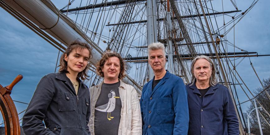 Portrait photo of the band Blue Machine, featuring the group of four stood on board historic ship Cutty Sark