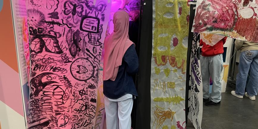 Young people attach brightly coloured pieces of painted fabric to a suspended washing line