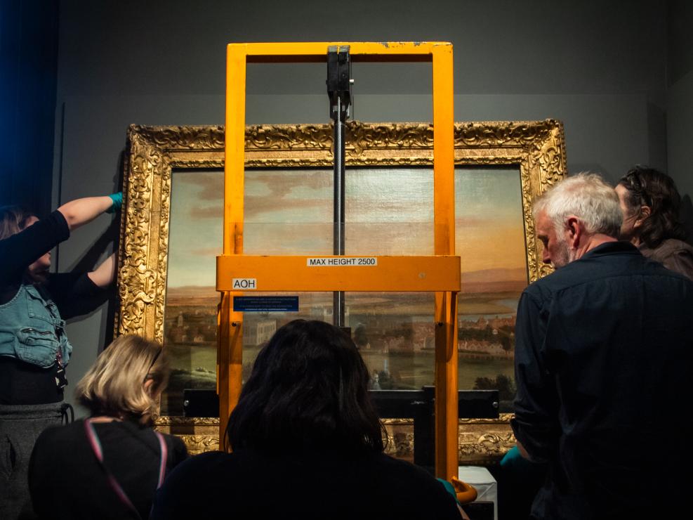 Art object handlers use a stacker truck to lift a heavy oil painting into place
