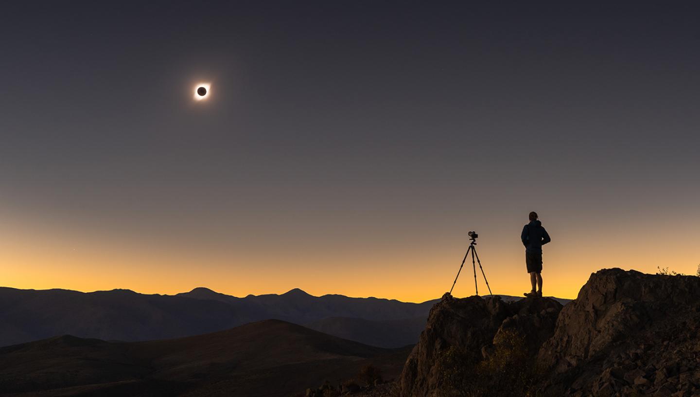 Image of person and a camera on a tripod taking a photo of the solar eclipse
