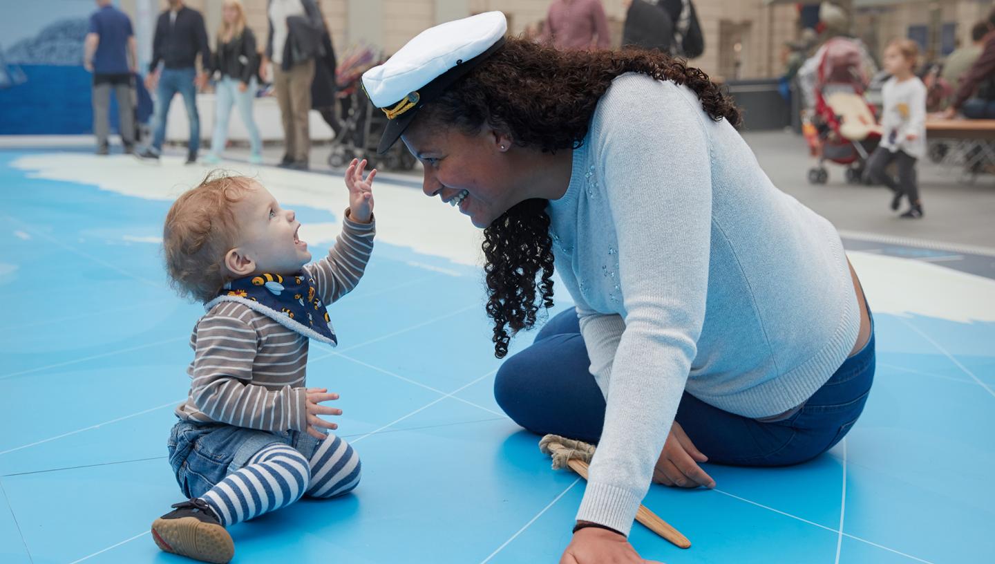A mother and her child play on the Great Map in the National Maritime Museum. The mother has a sailor hat on