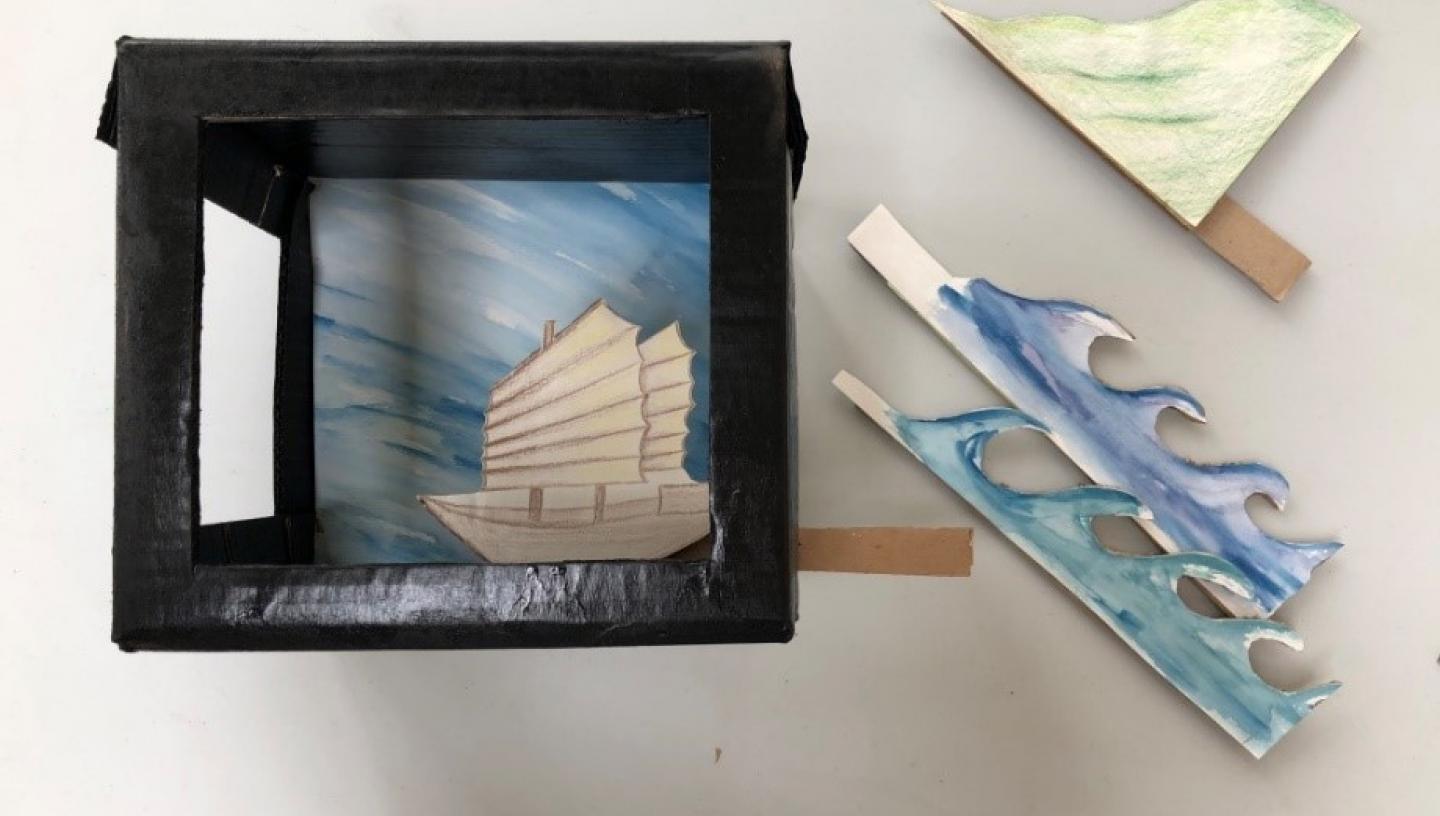 recycled box painted black to make a theatre with different props including a boat and come waves