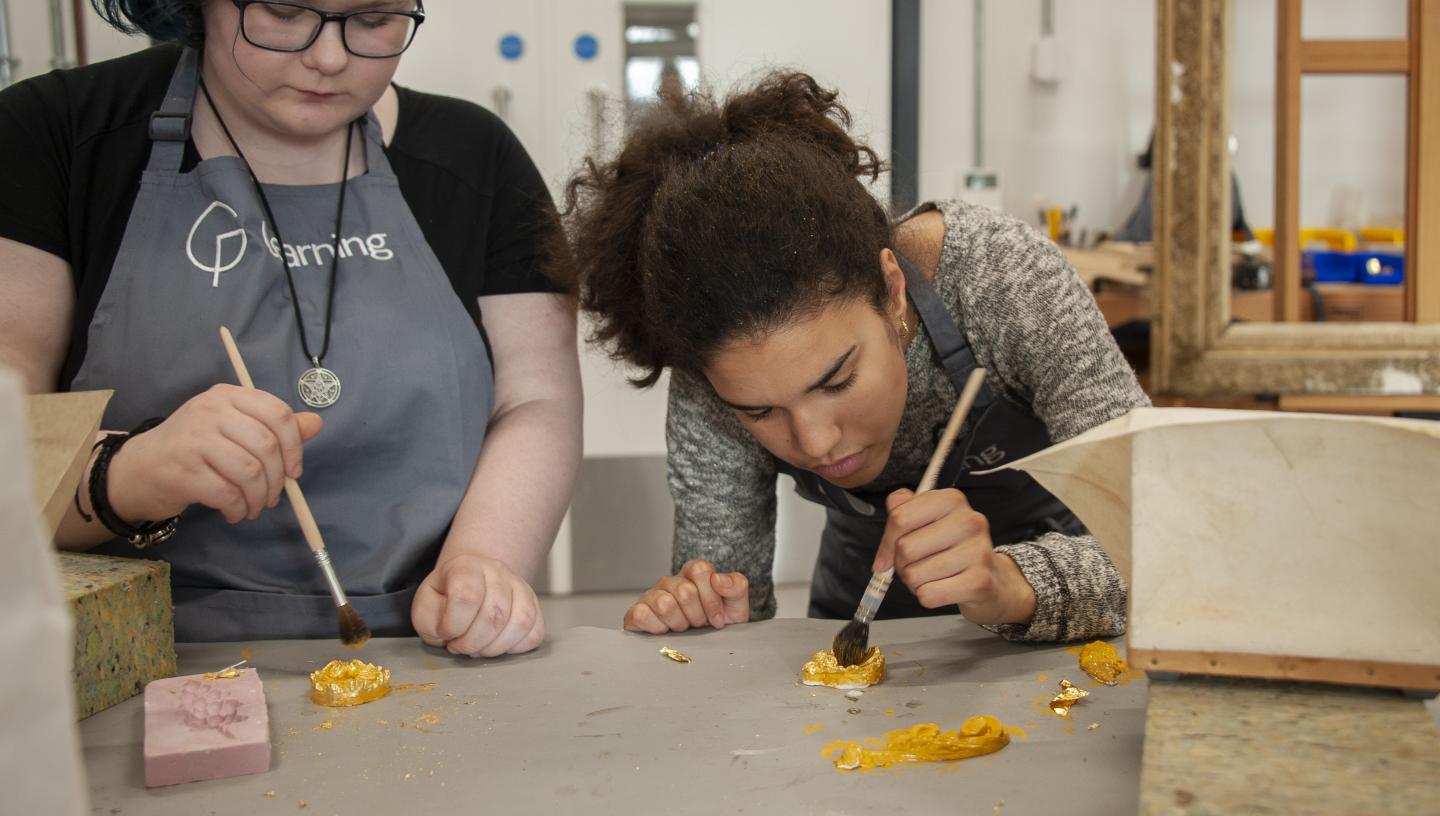 Two young people are painting gold leaf during a work experience placement