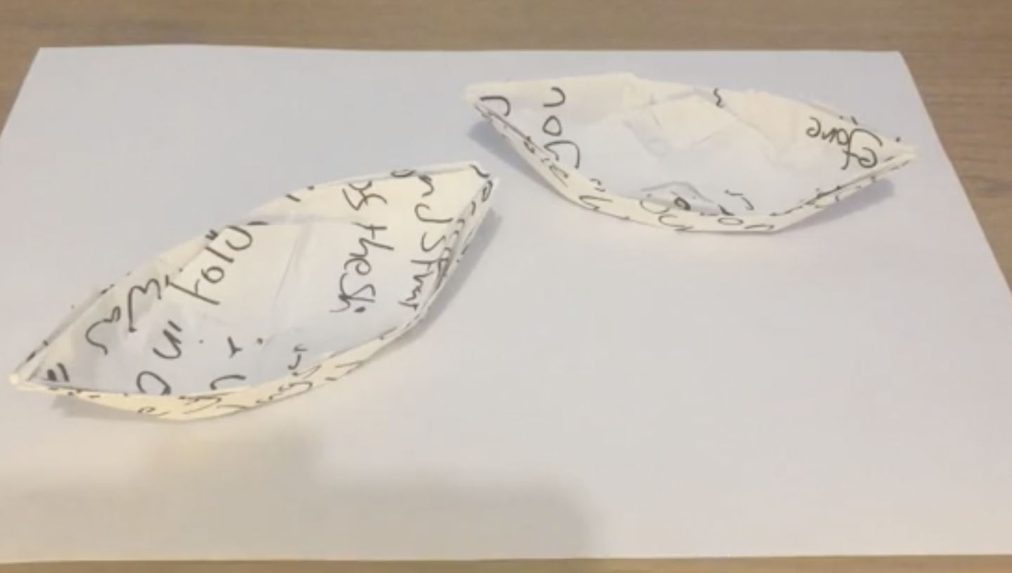 2 ships folded out of paper using origami. There is some illegible writing on the paper.