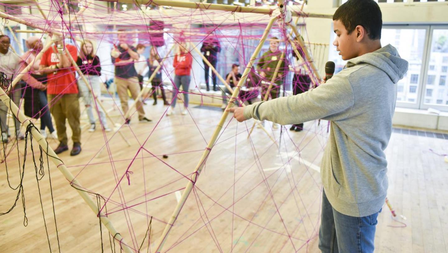  a young person is speaking on a mic in front of a sculpture