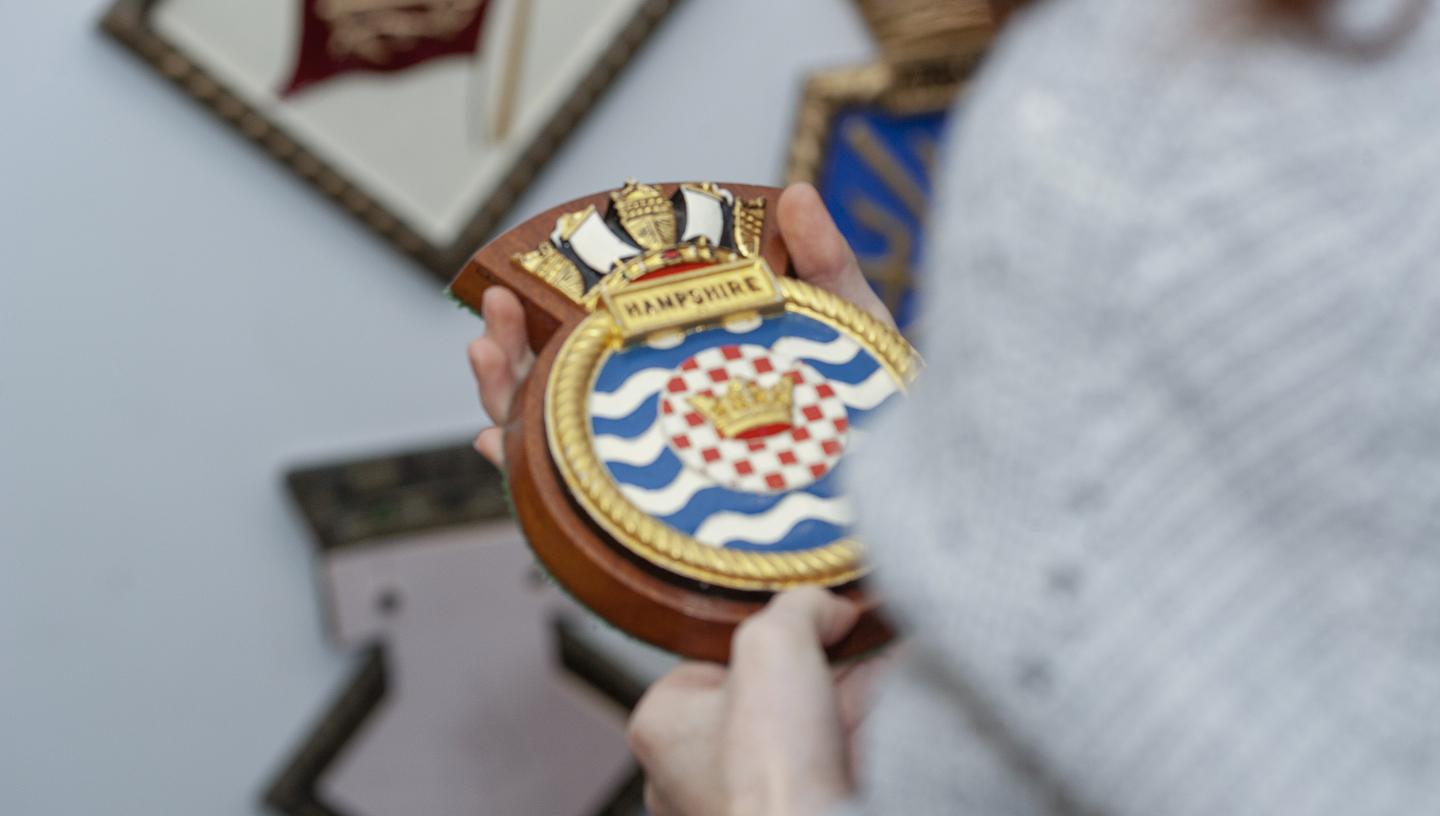 Someone holds a ship's badge to look at. The badge has a gold outline with blue and white wavy lines. 