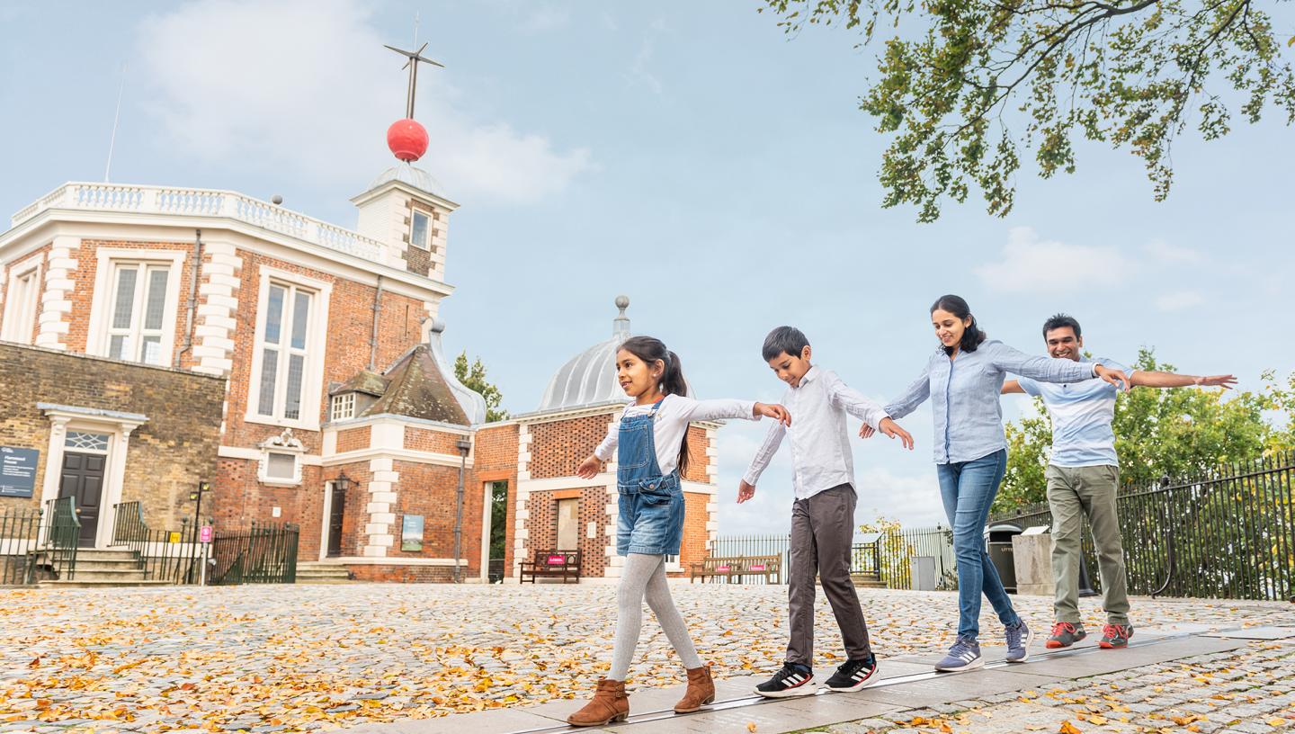 A family plays on the Prime Meridian Line in front of the historic buildings of the Royal Observatory