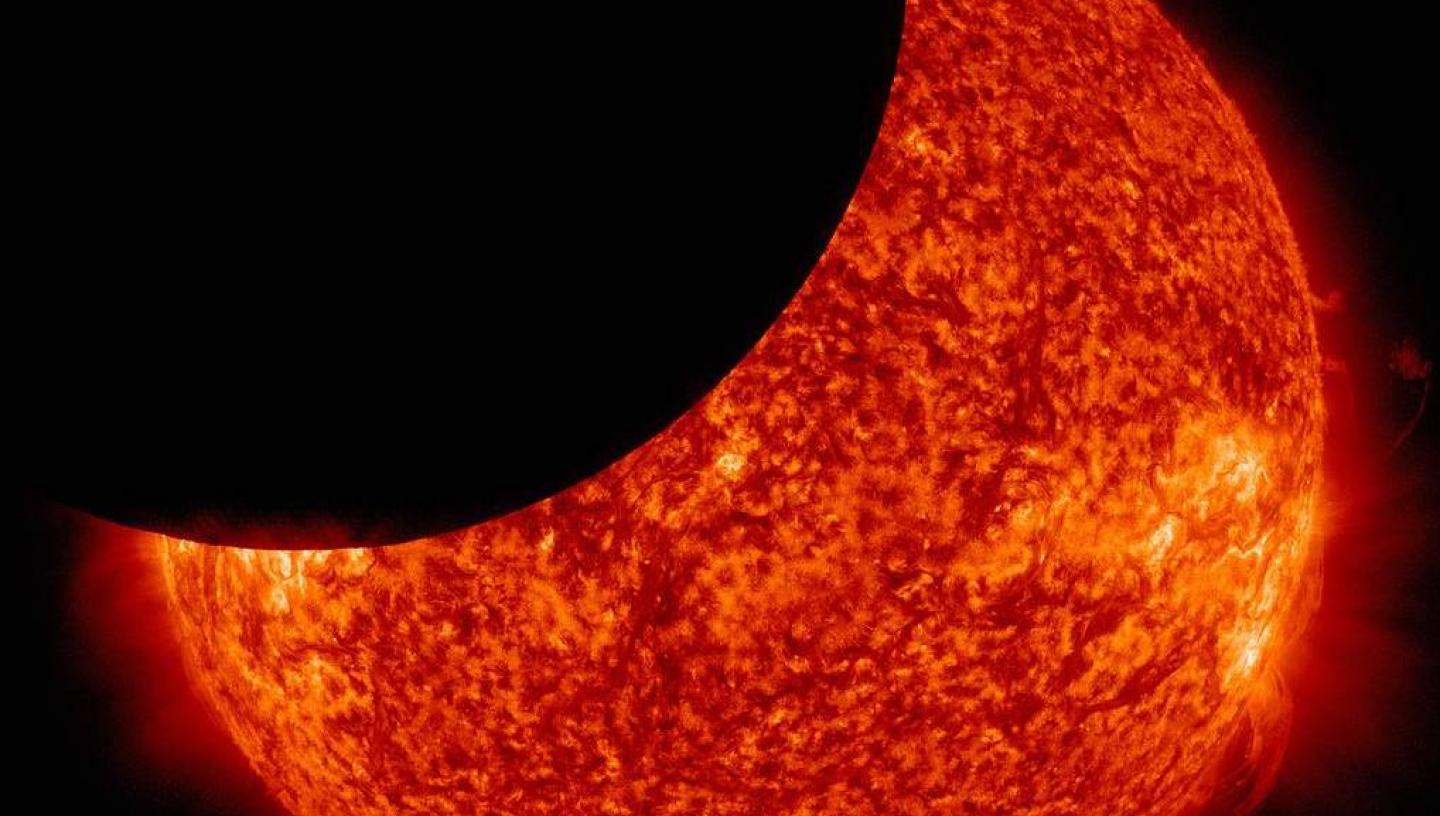 A telescope view of a partial solar eclipse, with the black shadow of the Moon crossing the fiery red disc of the Sun